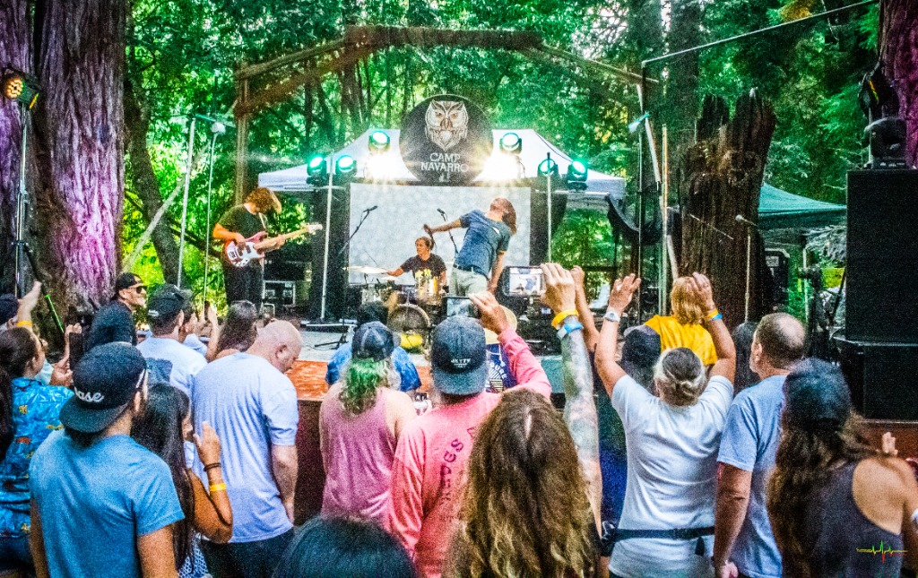 Daylight crowd cheering under towering California redwood trees at Camp Navarro.